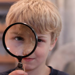 Photo of a child looking through a magnifying glass.
