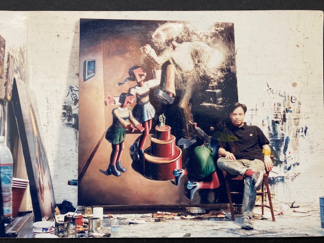 A photo of Evri Kwong sitting in a chair next to a large painting.